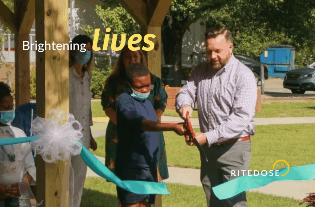 jody chastain and a teen boy cut a ribbon to celebrate the opening of a new pavilion for the homeless with text overlay: brightening lives